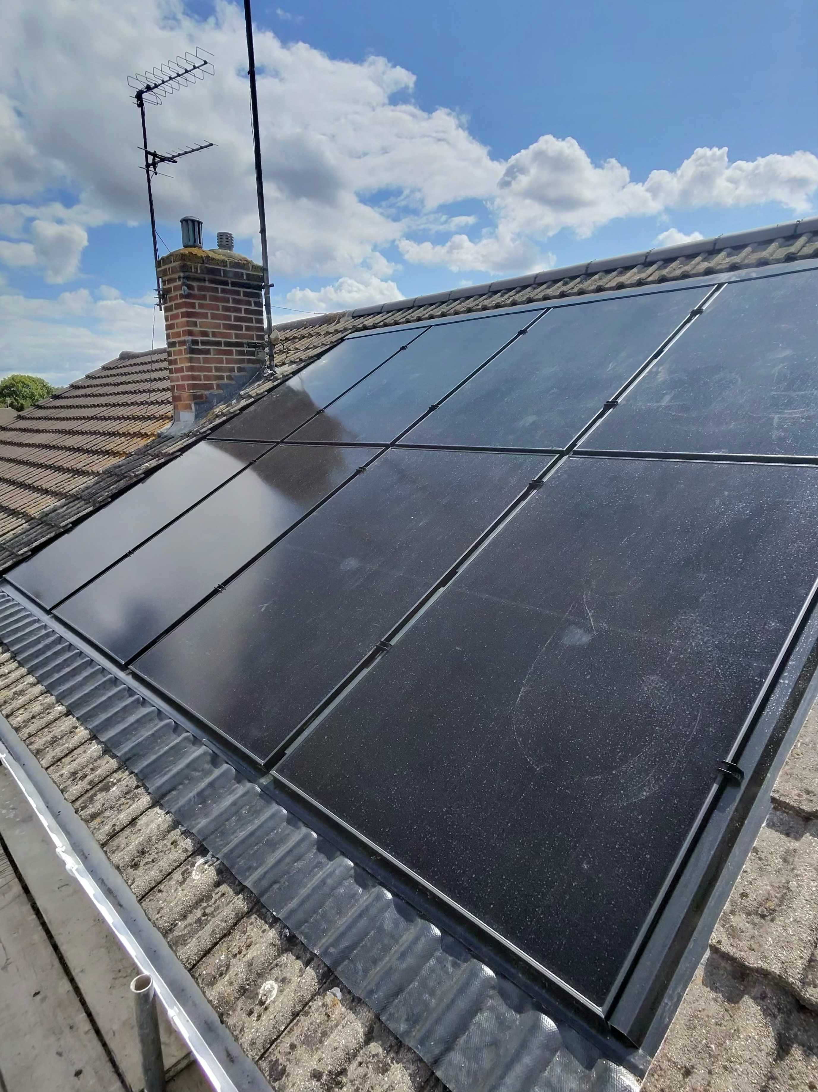 Black solar panels fitted to a residential roof beneath a blue sky